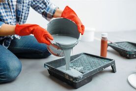 A pot of grey paint, being poured into a tray by a painter decorator.